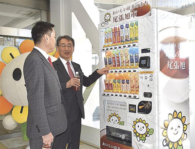 紅茶専用自動販売機の前で商品を選ぶ柴田市長（右）と小林執行役員